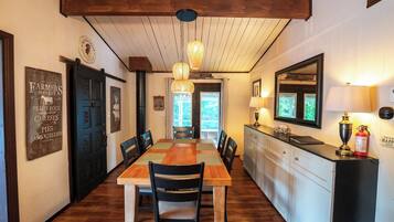 Uma sala de jantar com uma mesa e cadeiras de madeira, uma cozinha com bancada e armários, e um teto com vigas aparentes.