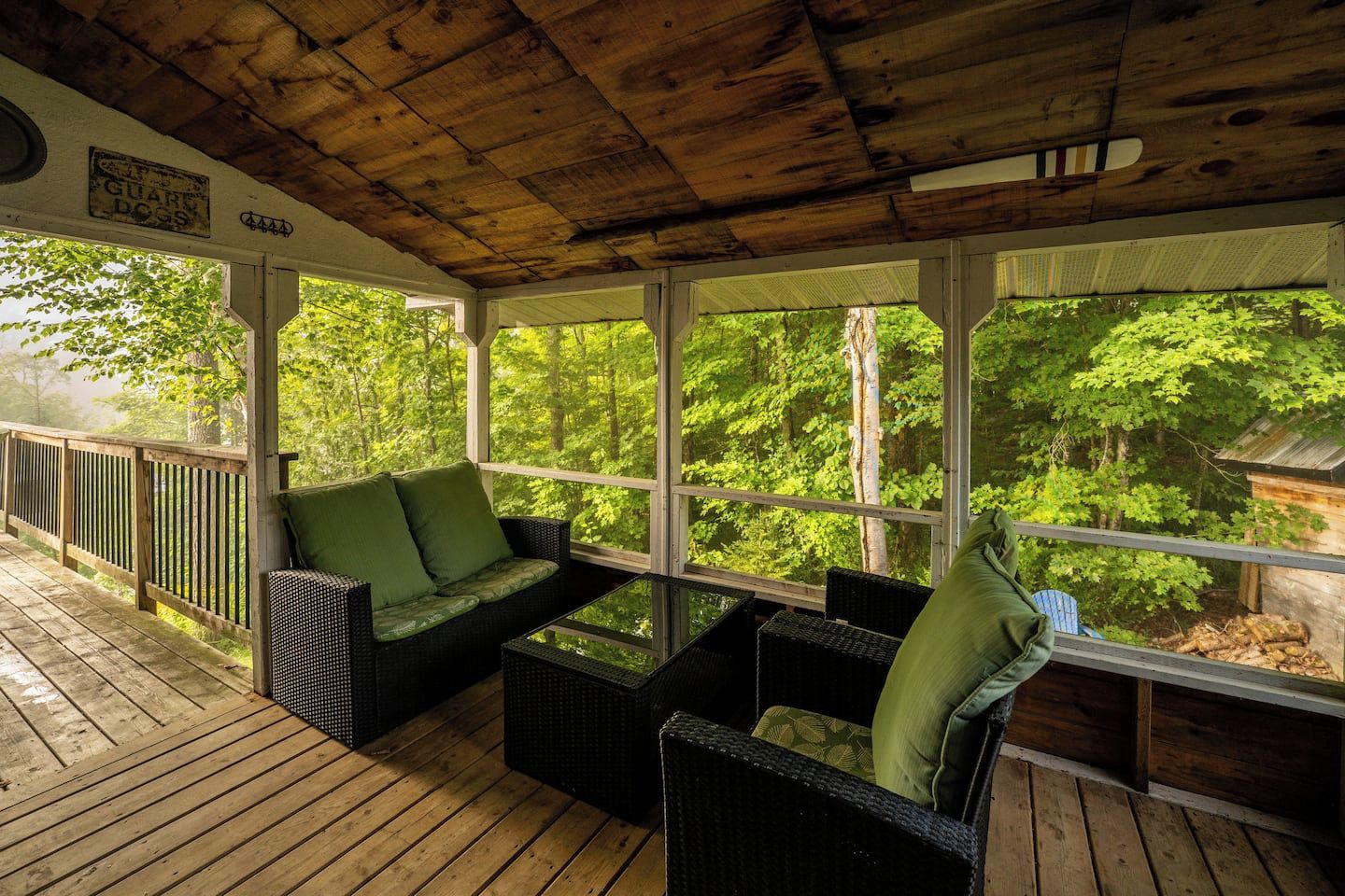 A covered outdoor seating area with wicker furniture and a view of a forest.
