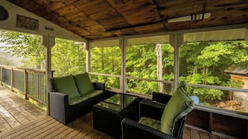 A covered outdoor seating area with wicker furniture and a view of a forest.