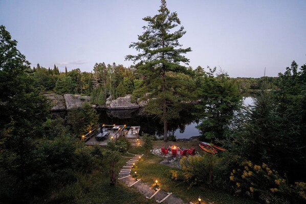 A lakeside outdoor area with a dock, seating, and a fire pit.