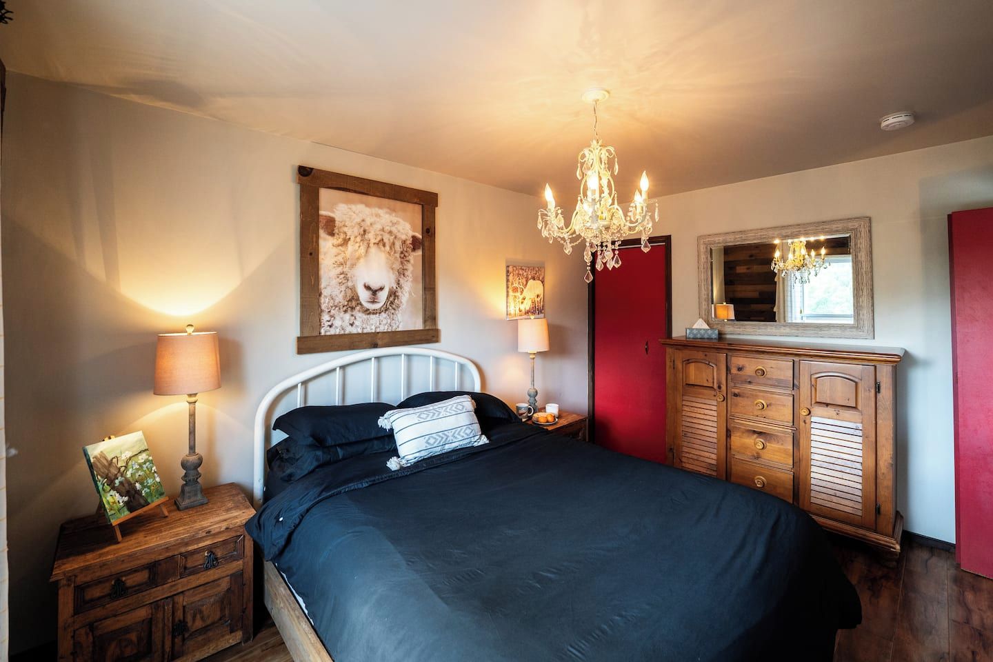 A bedroom with a bed, bedside lamps, a dresser, a mirror, and a chandelier.