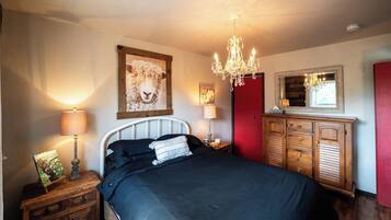 A bedroom with a bed, bedside lamps, a dresser, a mirror, and a chandelier.