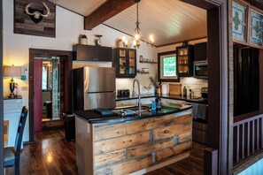 Cozinha com ilha central, eletrodomésticos de aço inoxidável, armários de madeira e luminária pendente.