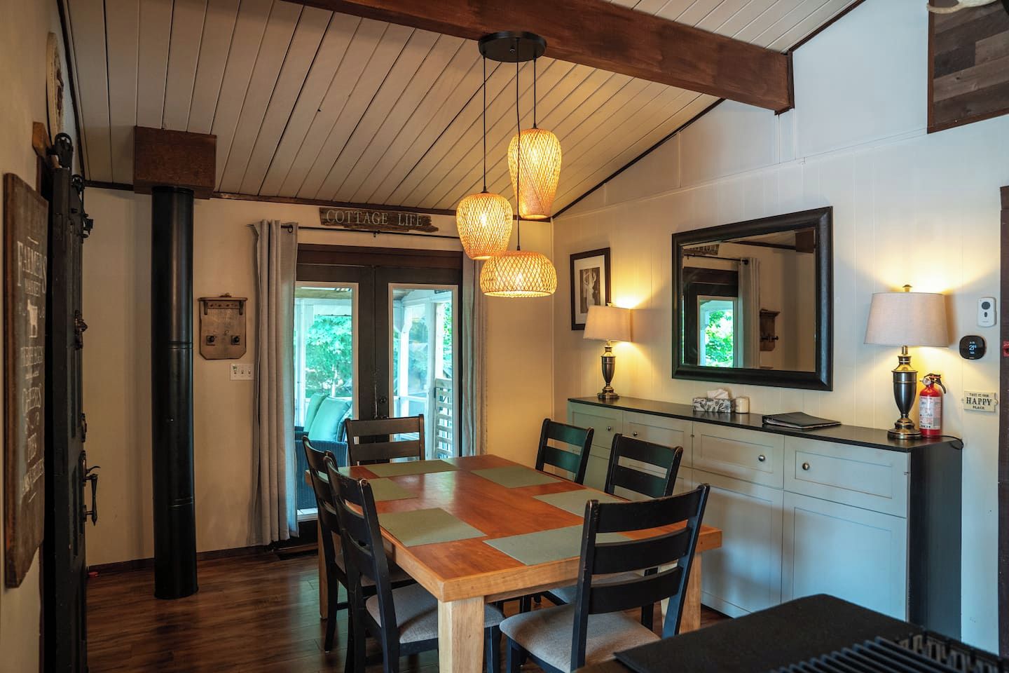 Un comedor con mesa y sillas de madera, luces colgantes, un espejo y un letrero que dice 'COTTAGE LIFE'.