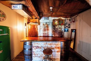 Um espaço de bar rústico com balcão de madeira, uma geladeira verde antiga e uma placa na parede com a inscrição 'MARG Z'.