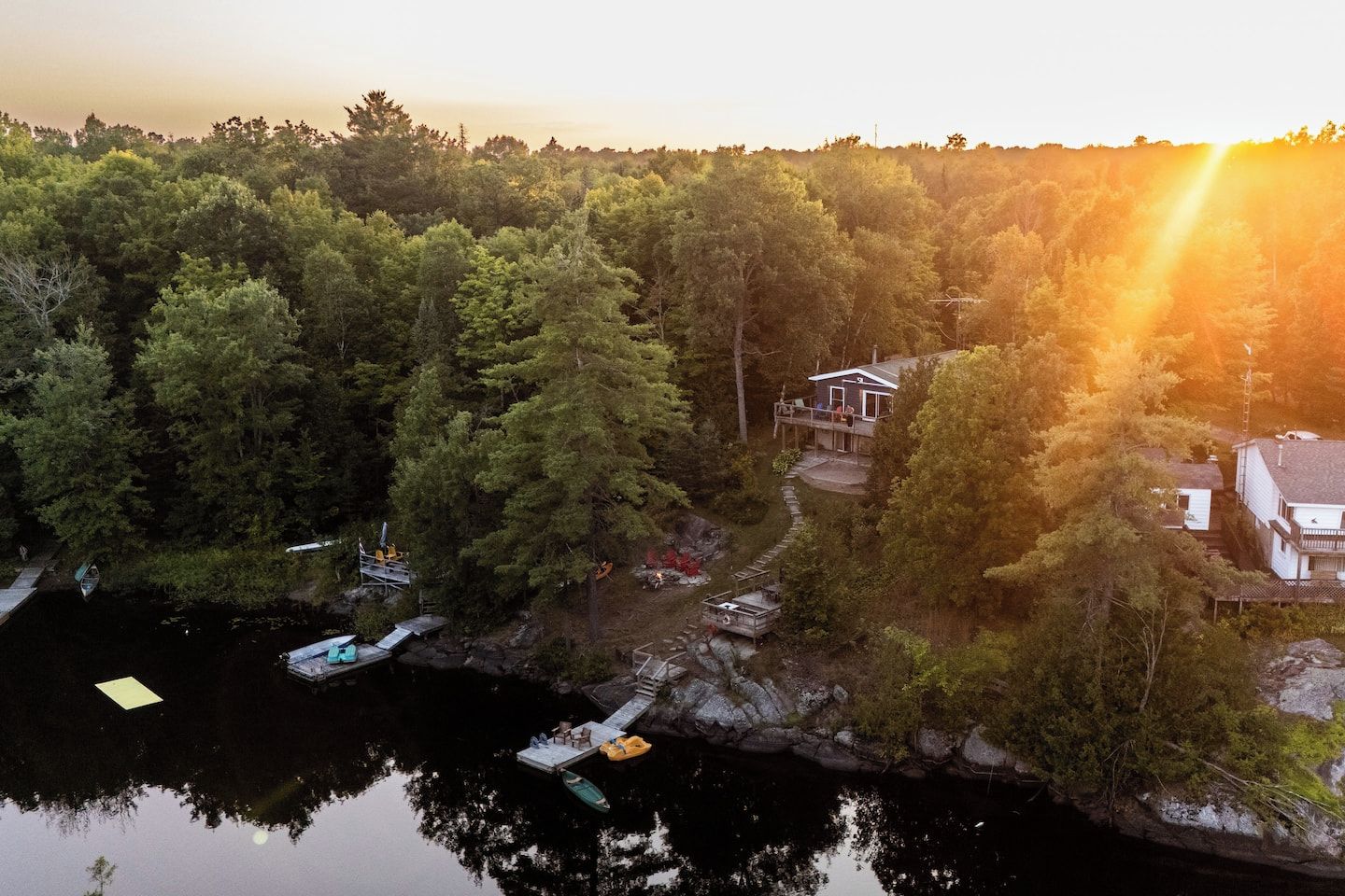 A lakeside property with a dock, boats, and a house surrounded by dense forest.