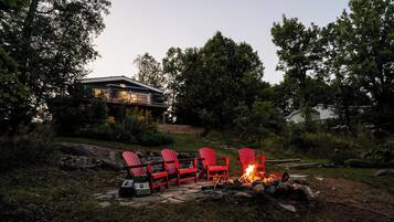 Eine Terrasse mit roten Adirondack-Stühlen und einer Feuerstelle, umgeben von einer natürlichen Landschaft und einem Haus im Hintergrund.