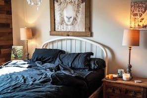 Un dormitorio con una cama, dos lámparas de noche, una mesita de noche con una vela y un cuadro en la pared.