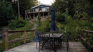 A wooden deck with a table and chairs, a covered area with a blue canopy, and a house in the background.