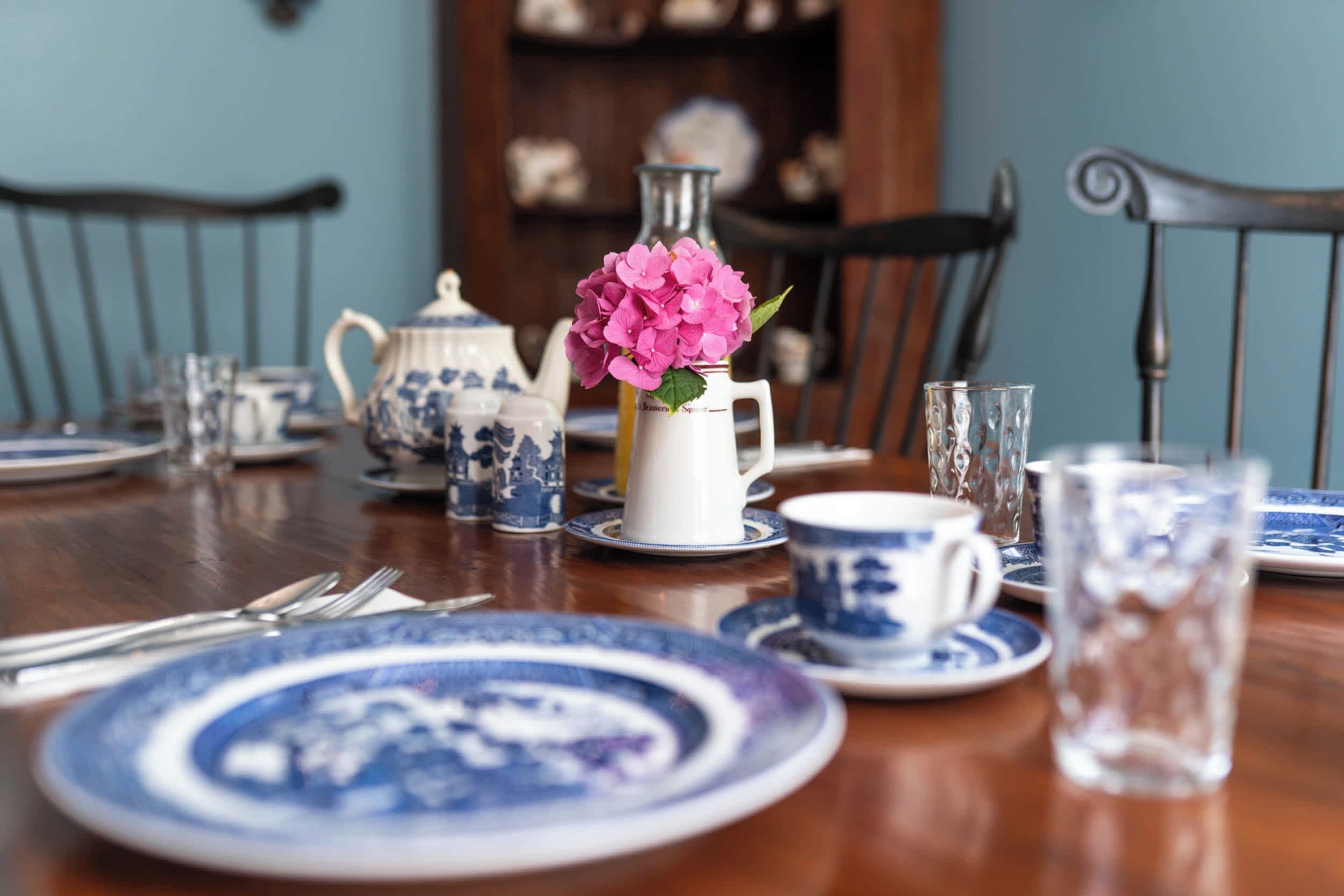 A dining table set with blue and white porcelain dinnerware, including plates, cups, and a teapot.