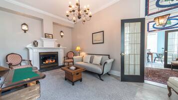 Uma sala de estar com lareira, um candelabro, um sofá e um espaço de jantar com cadeiras.