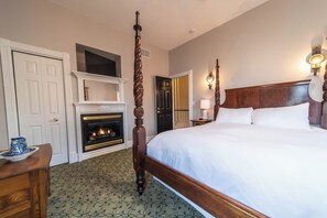 Une chambre d’hôtel avec un lit à baldaquin, une cheminée, une porte et un luminaire fixé au mur.