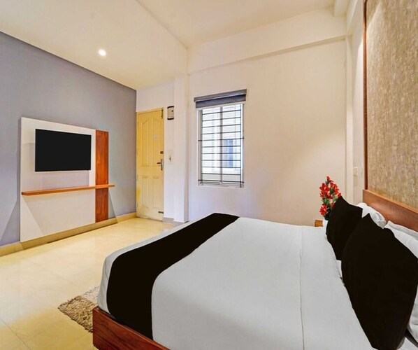 A bedroom with a bed, a TV mounted on the wall, a window with blinds, and a door.