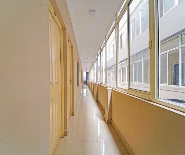 A long, narrow hallway with doors on one side and windows on the other, leading to an open area.