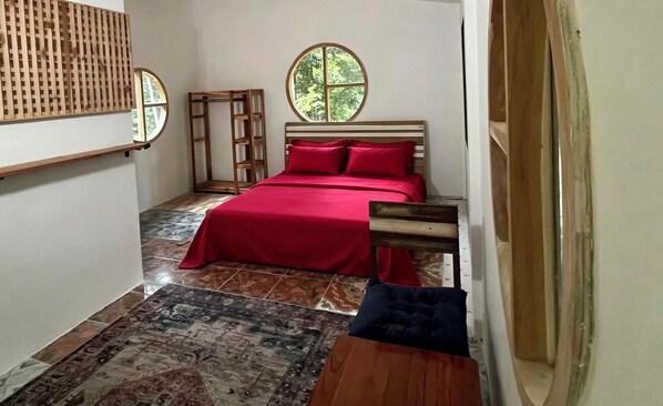 A bedroom with a bed, a window, a wooden headboard, and a patterned rug.