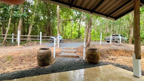 A covered outdoor area with a gravel path leading to a white fence, surrounded by trees.