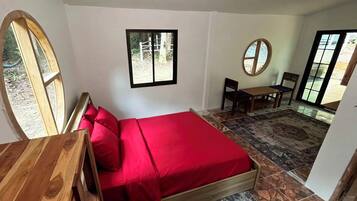 A bedroom with a bed, a desk, a chair, a small table, and a window.