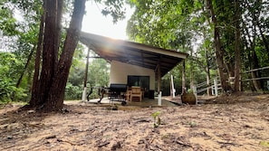A rustic wooden cabin with a covered patio, surrounded by dense forest.