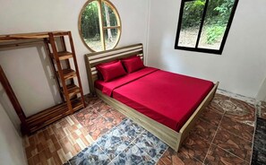 Une chambre avec un lit, une échelle en bois, un miroir rond et une fenêtre donnant sur un paysage verdoyant.