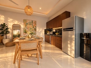 A modern kitchen with a dining area, featuring a large wooden table, a hanging light fixture, and a refrigerator. - Private Pool Villa, Central Canggu (Badung)