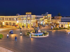 Un hotel con una glorieta central, una estatua y varios edificios con letreros iluminados.