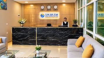 A hotel reception area with a marble reception desk, a receptionist, and a sofa with cushions.