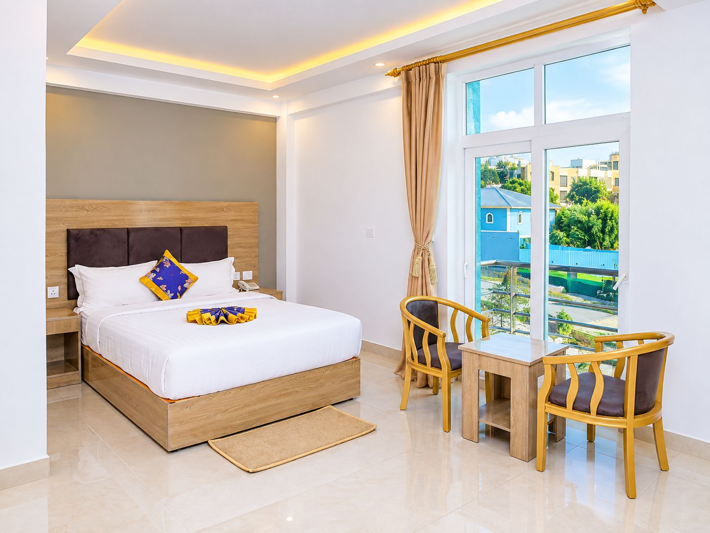 Quarto de hotel com cama, mesa de cabeceira, duas cadeiras, janela com vista e uma pequena varanda.