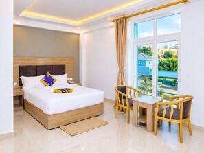 Habitación de hotel con cama, mesita de noche, dos sillas, ventana con vistas y un pequeño balcón.
