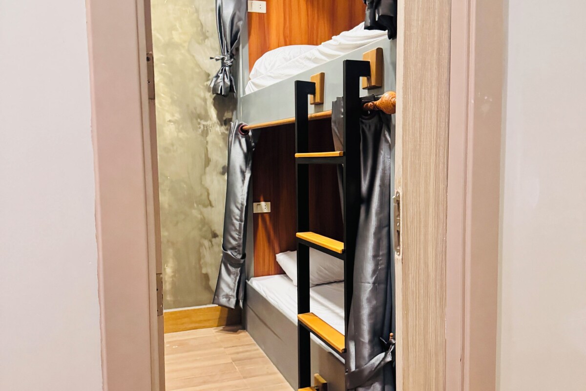 A narrow hallway leading to a room with a bunk bed, wooden walls, and a curtain.