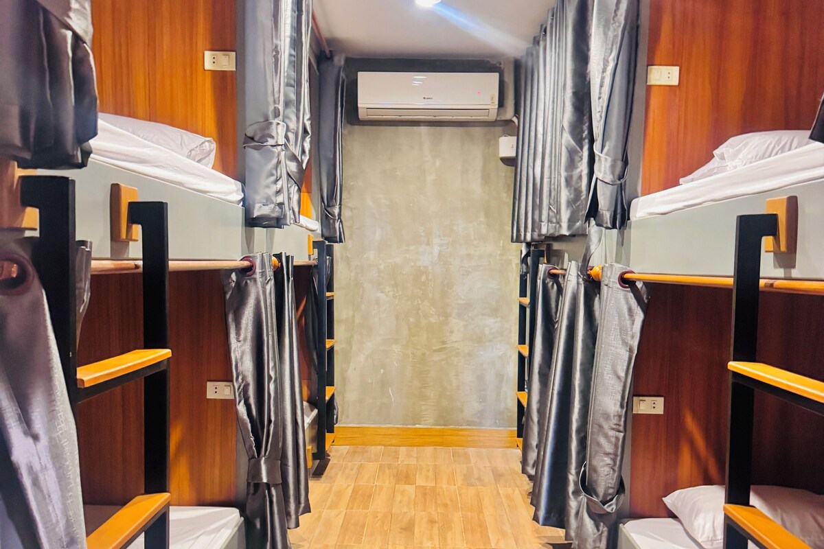 A corridor with bunk beds, wooden flooring, and an air conditioning unit on the wall.