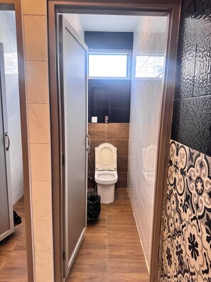 A narrow bathroom with a toilet, a shower, and a window. - Lao Smart Box Hostel (Vientiane)