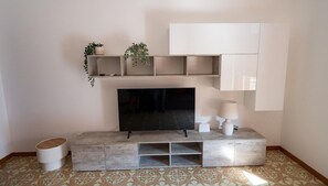 Uma sala de estar com televisão de tela plana, lareira, mesa de centro e estante com plantas.