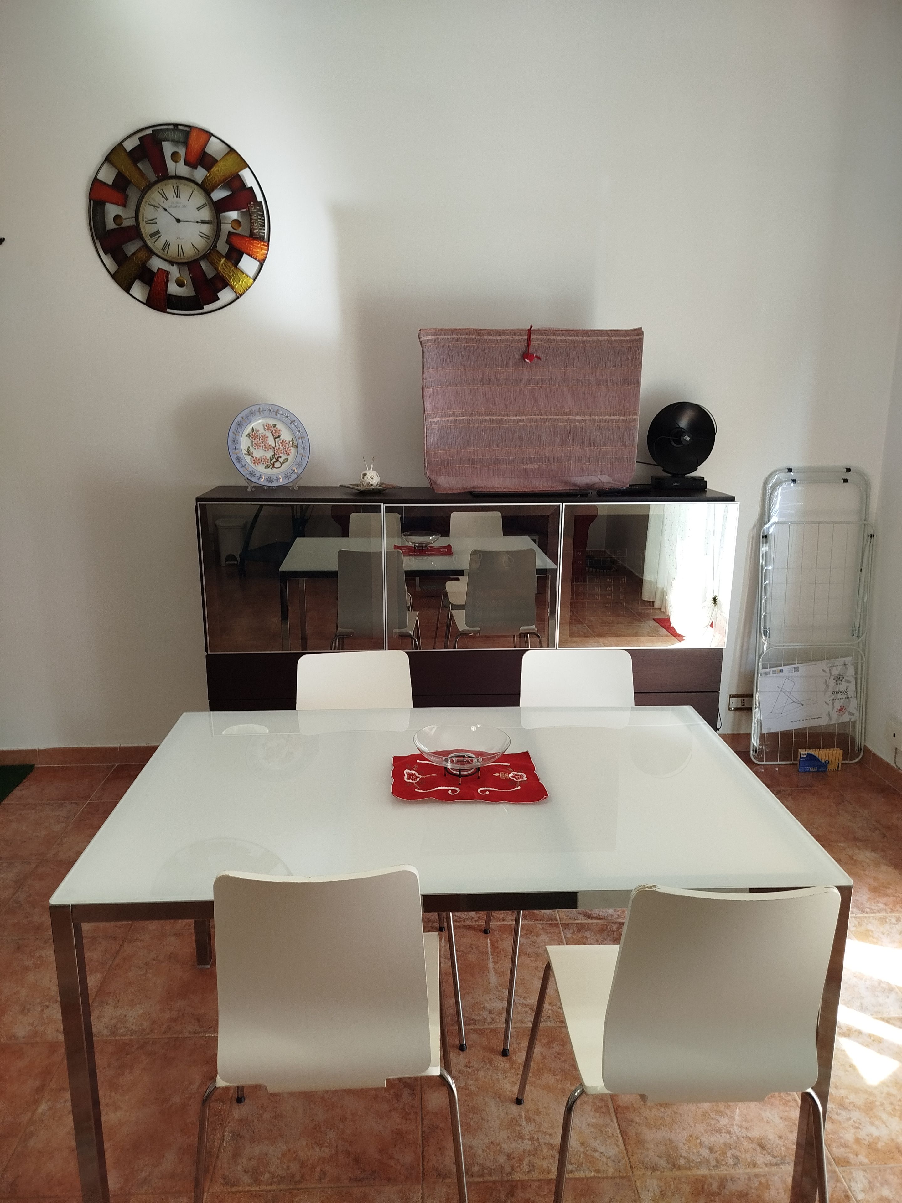 Un coin repas avec une table blanche, quatre chaises, une horloge décorative, une petite assiette et un radiateur.