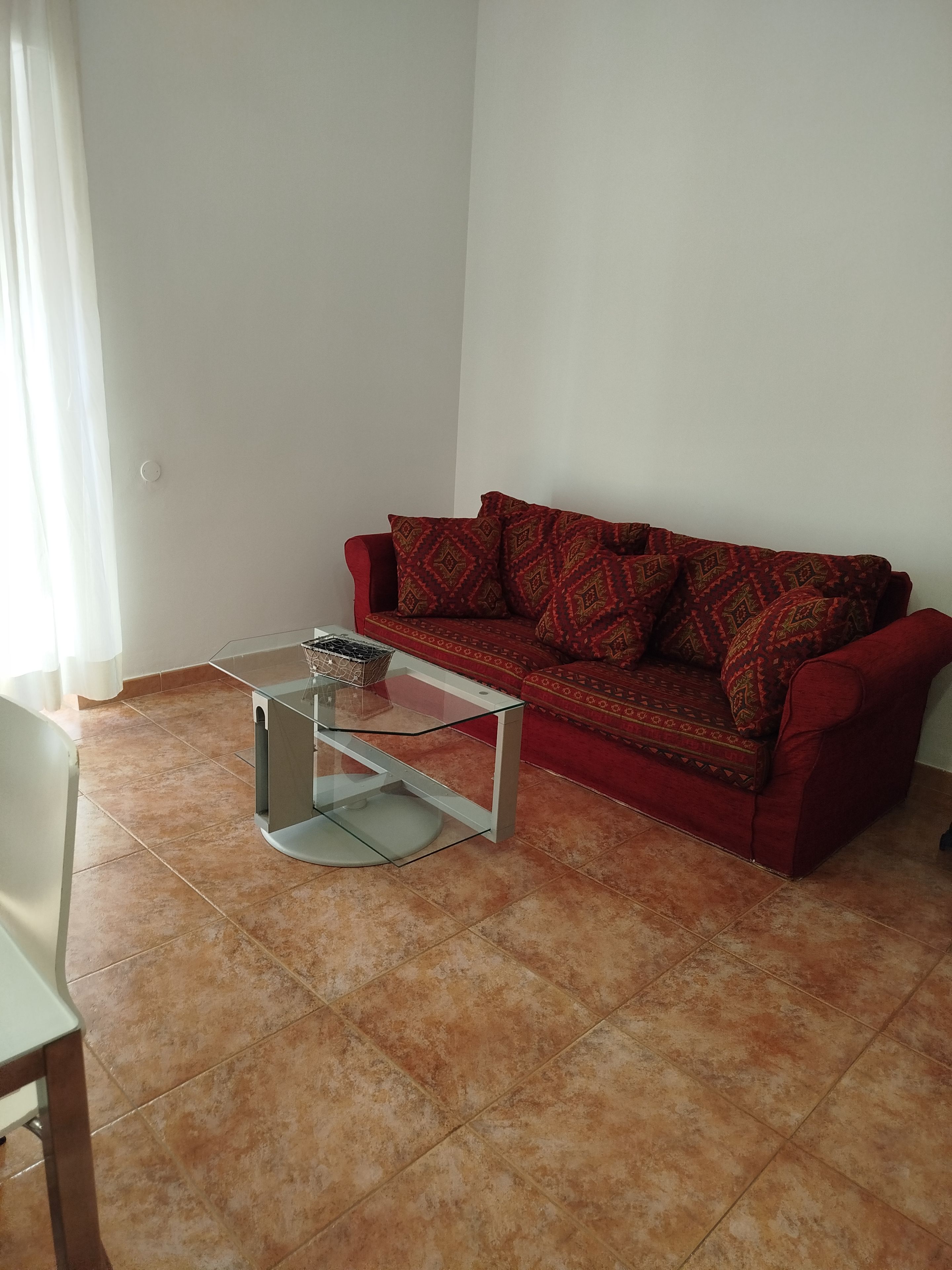 Un salon avec un canapé rouge, une table basse en verre et un sol carrelé.