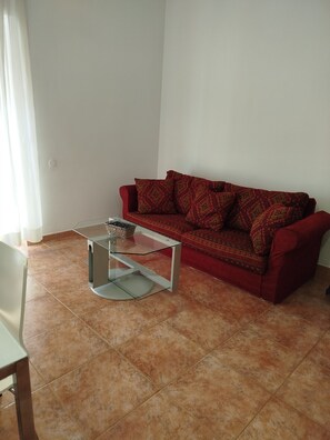 Ein Wohnzimmer mit einem roten Sofa, einem Glastisch und einem Fliesenboden.