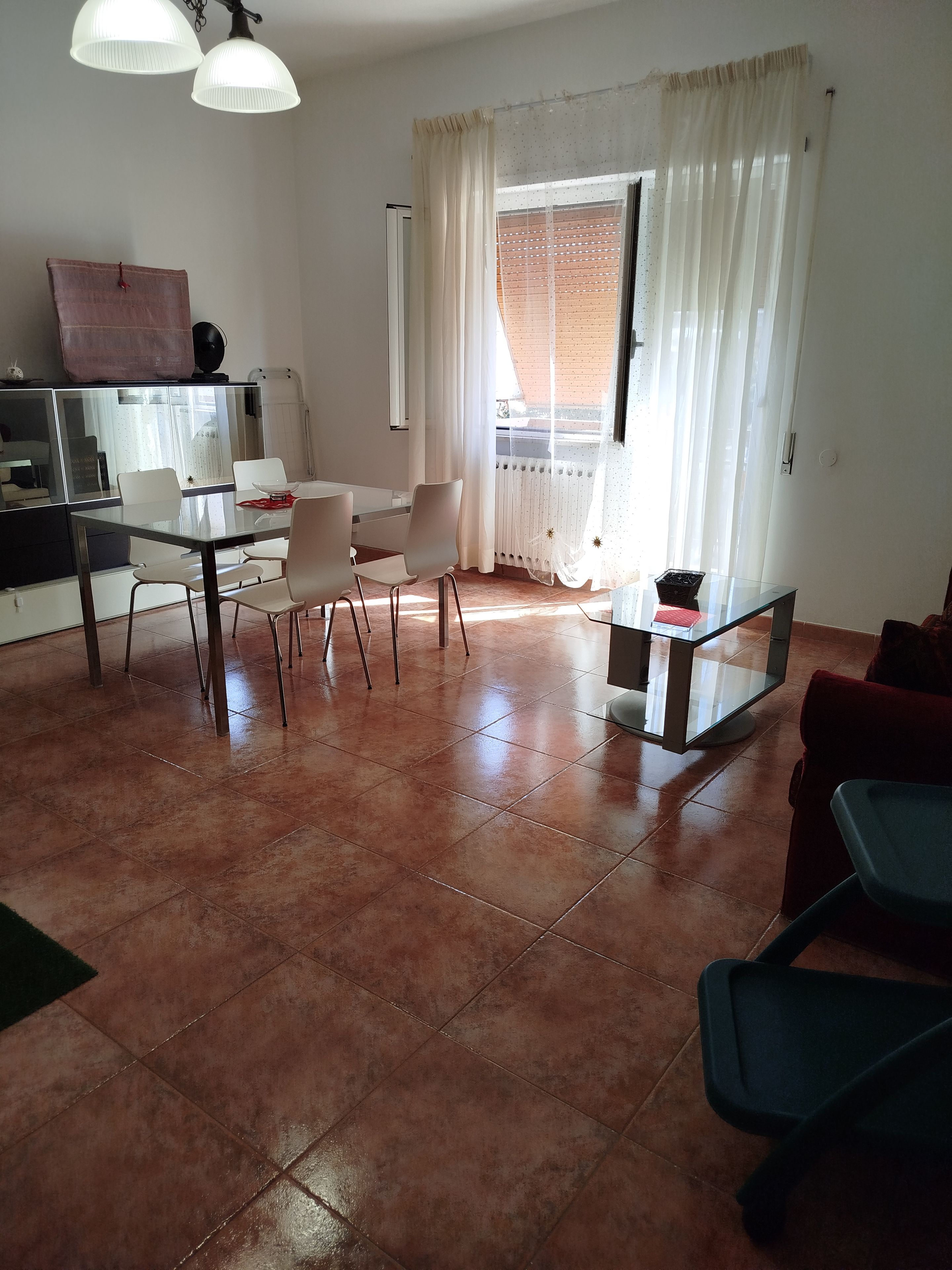 Un salon avec une table à manger en verre, des chaises blanches, un canapé rouge et un téléviseur posé sur un meuble.