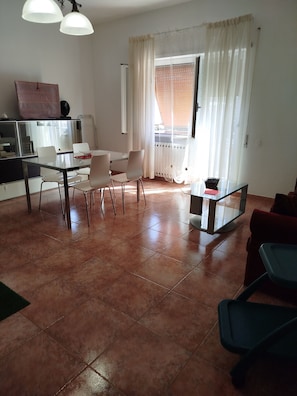 Ein Wohnzimmer mit einem Glastisch, weißen Stühlen, einem roten Sofa und einem Fernseher auf einem Schrank.