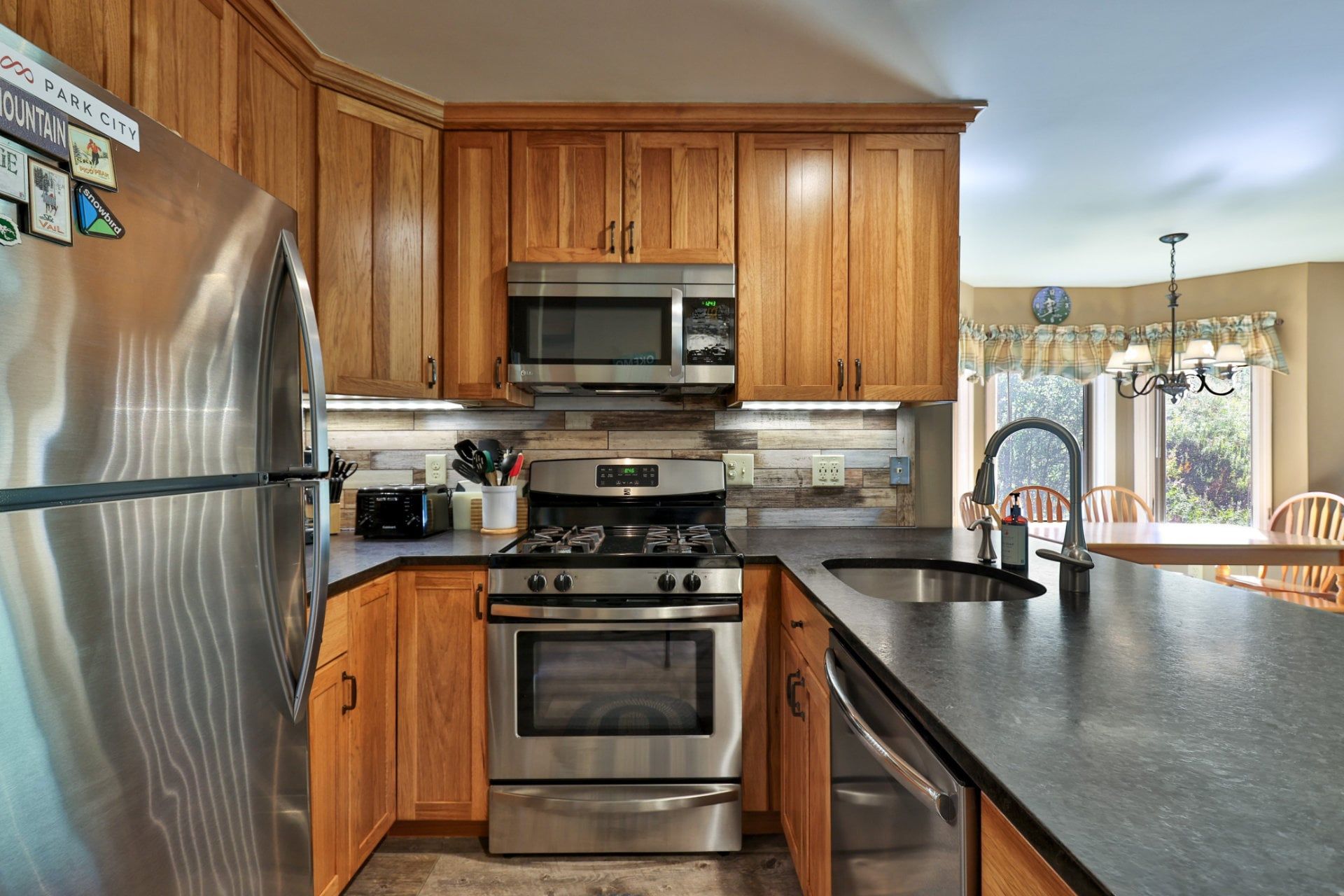 A kitchen with wooden cabinets, stainless steel appliances, a microwave, stove, oven, and a sink.
