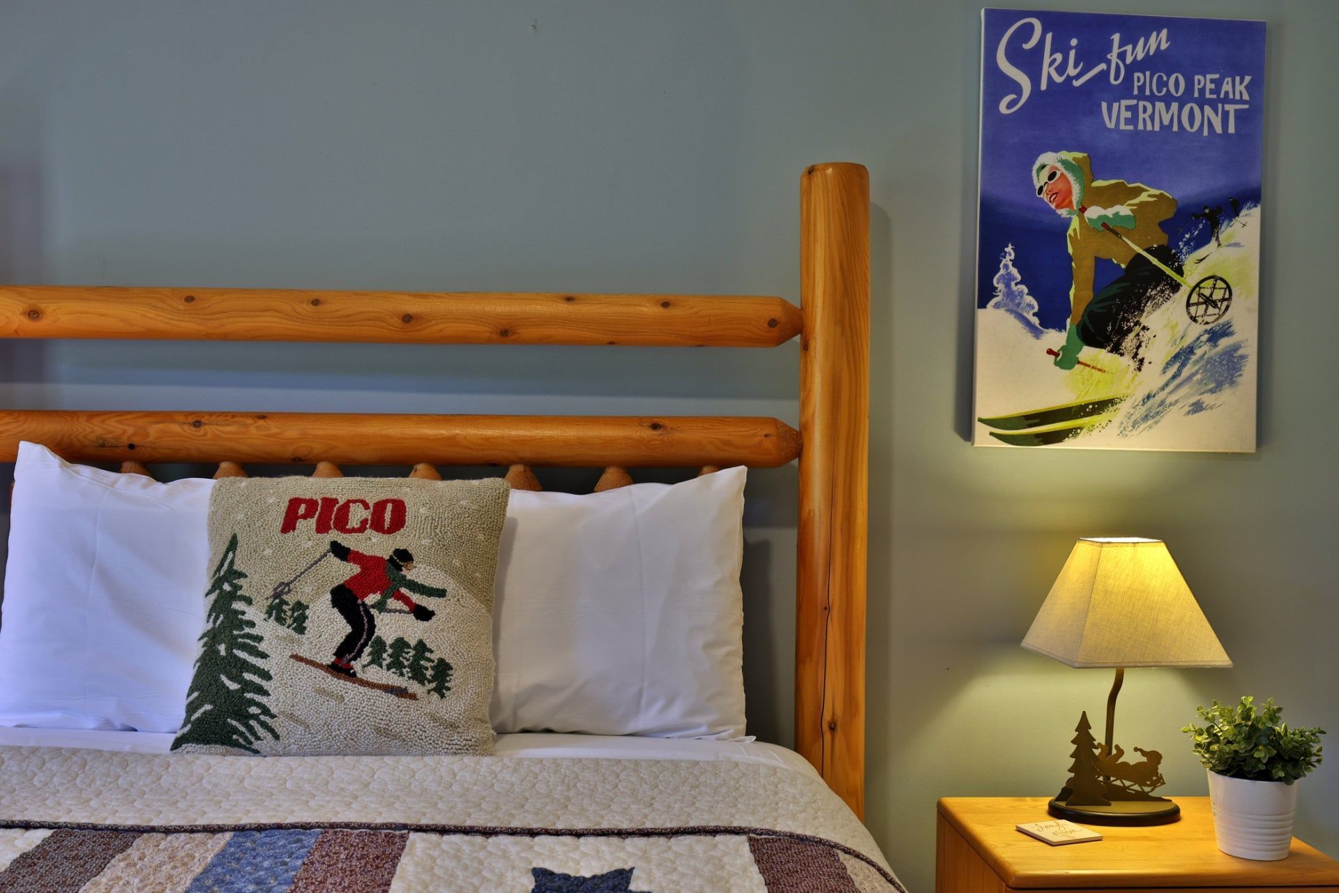 A bedroom with a wooden headboard, a quilted bedspread, a pillow with a ski-themed design, a wall-mounted lamp, and a poster of a skier.