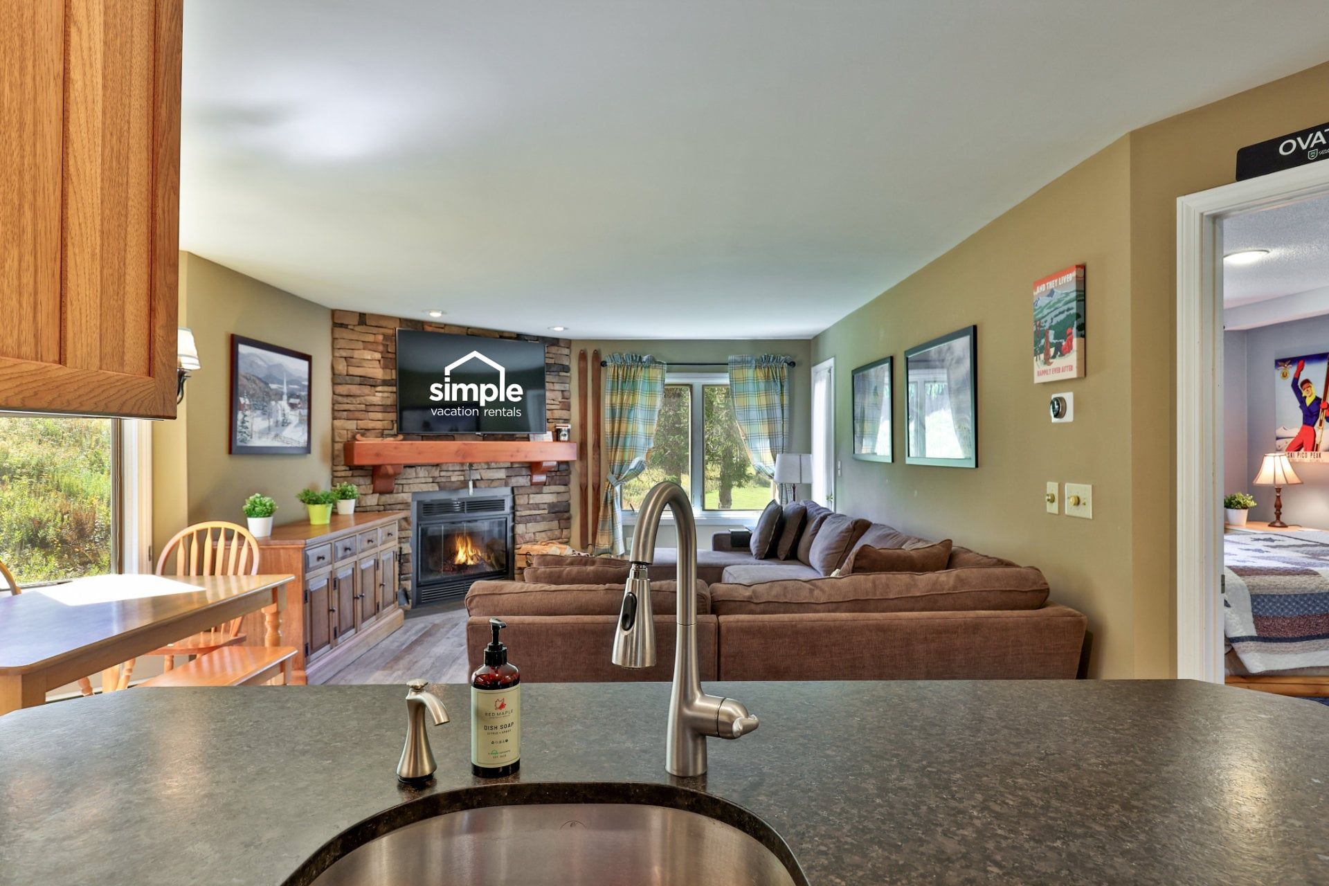 A modern living room with a fireplace, a sofa, a dining area, and a kitchen counter with a sink.