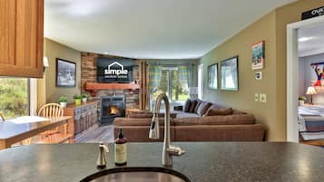 A modern living room with a fireplace, a sofa, a dining area, and a kitchen counter with a sink.