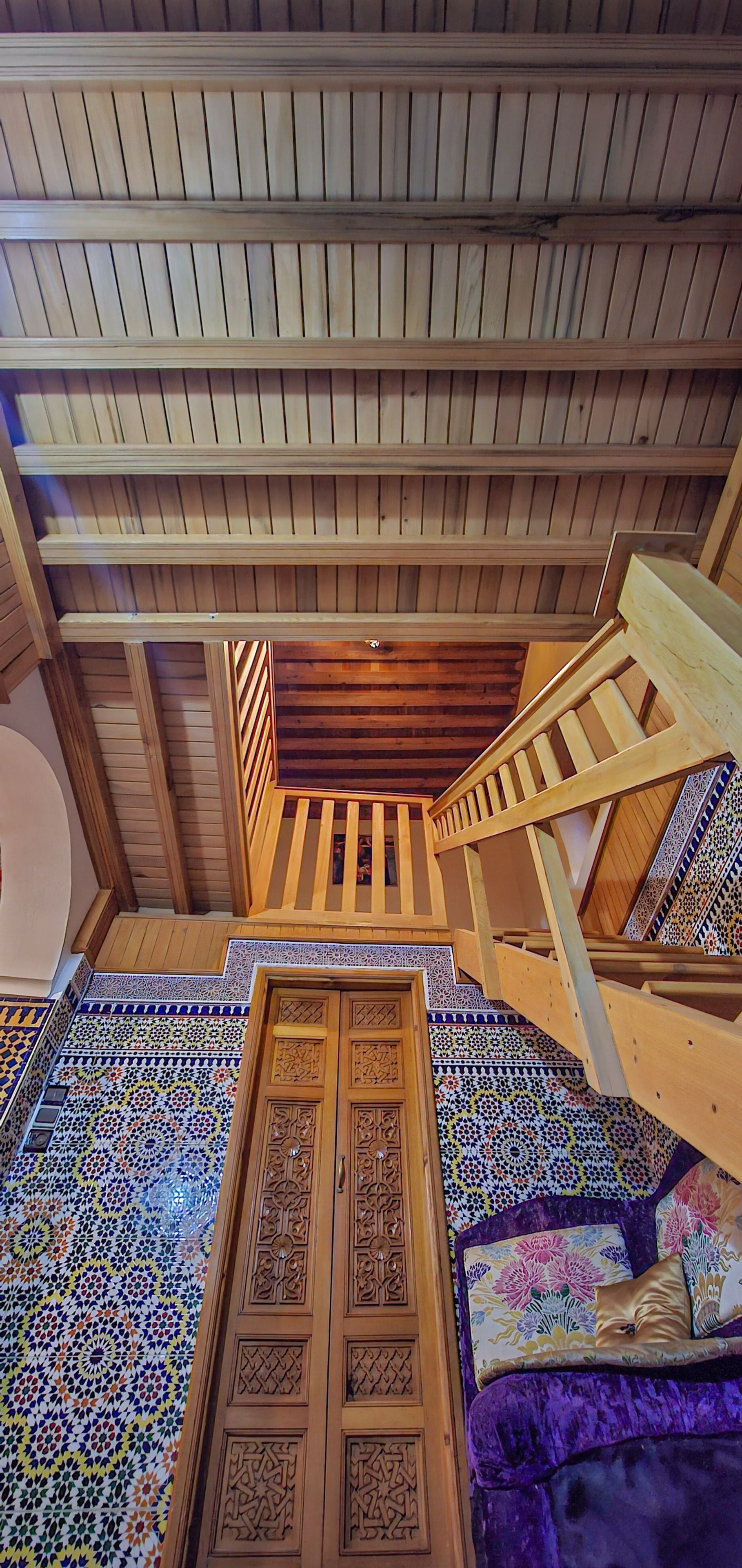 A room with a wooden ceiling, a staircase, and a door with intricate patterns.