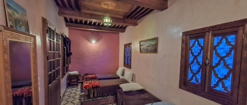 A narrow hallway with a wooden ceiling, a bed with a patterned bedspread, and a window with a geometric design.