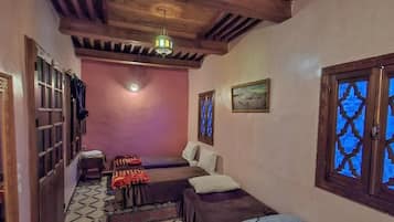 A narrow hallway with a wooden ceiling, a bed with a patterned bedspread, and a window with a geometric design.