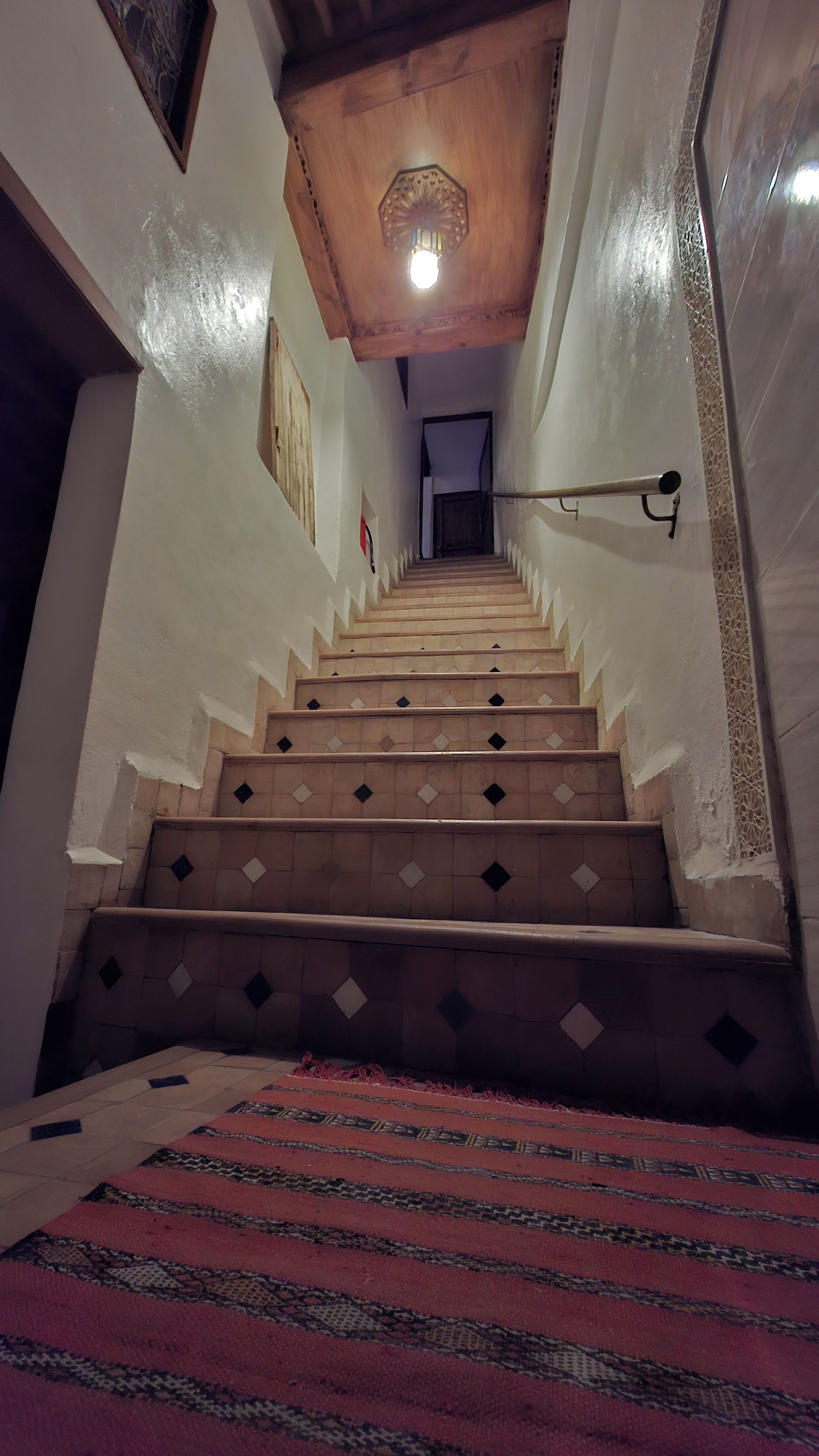 Eine Treppe mit gemusterten Fliesen und einer Handläufe, die zu einem Raum mit einem gemusterten Teppich führt.