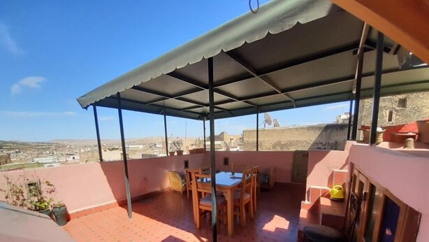 A covered outdoor seating area with a table and chairs, a tiled floor, and a view of the surrounding landscape. - Dar roeya (Fes)