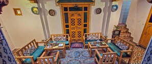 Quarto acolhedor com uma mesa de madeira central rodeada por cadeiras, um tapete estampado e uma porta de madeira decorativa.
