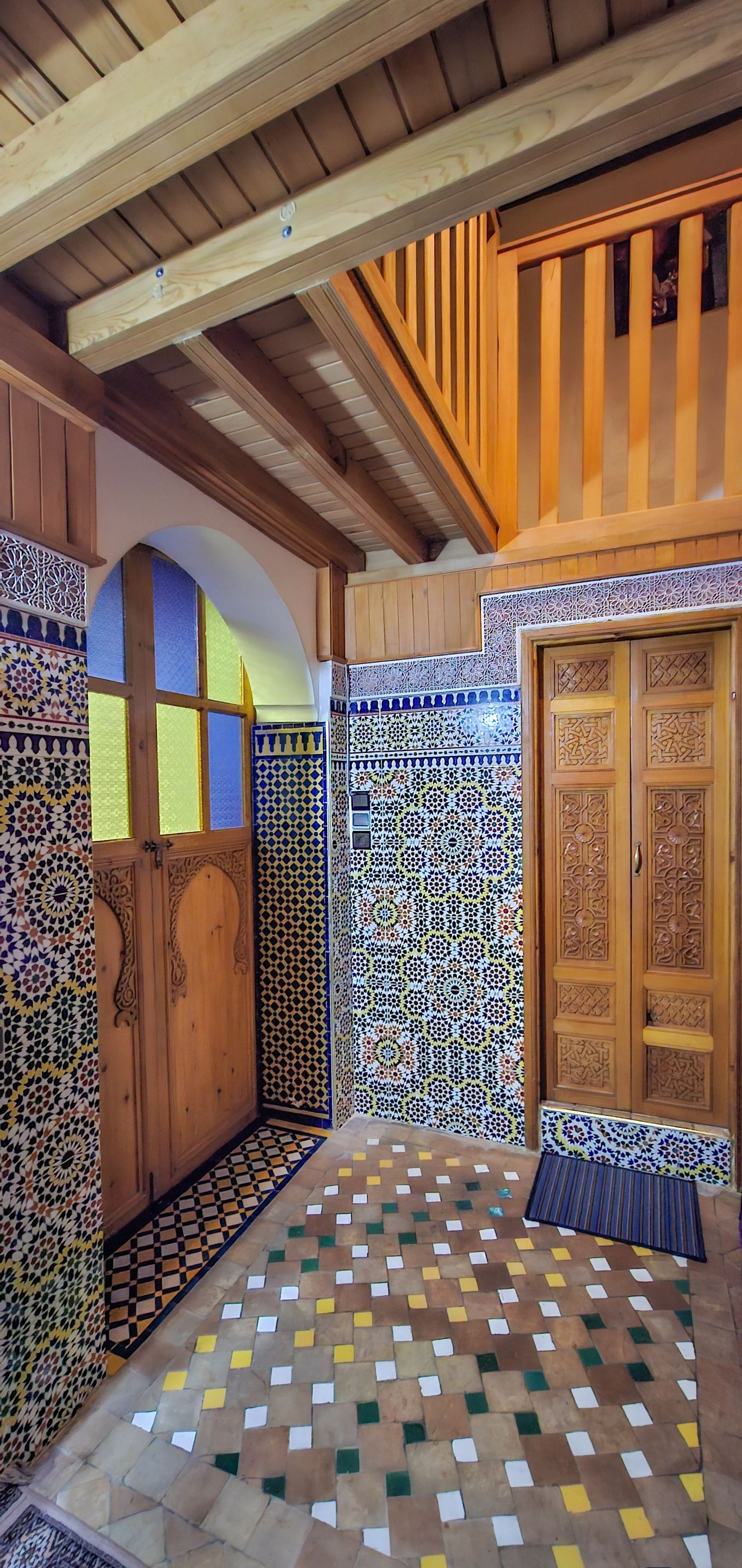 A room with a tiled floor, wooden door with intricate carvings, and a wooden ceiling with exposed beams.