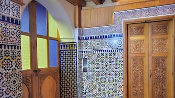 A room with a tiled floor, wooden door with intricate carvings, and a wooden ceiling with exposed beams.