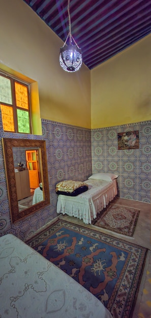 Una habitación con cama, espejo, lámpara colgante, paredes con diseño y alfombra.